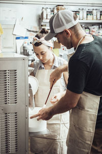 Colleagues using machinery while making ice cream at commercial kitchen