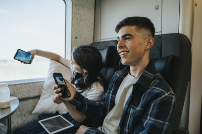Happy boy holding smart phone while sitting on seat in train