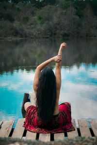 Rear view of woman with arms raised sitting on pier by sea