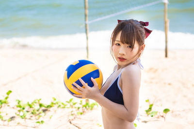 Portrait of beautiful woman holding ball on beach