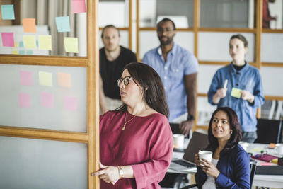 Confident businesswoman explaining business strategy over adhesive notes to colleagues in meeting