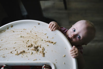 Portrait of toddler holding high chair with leftovers on it