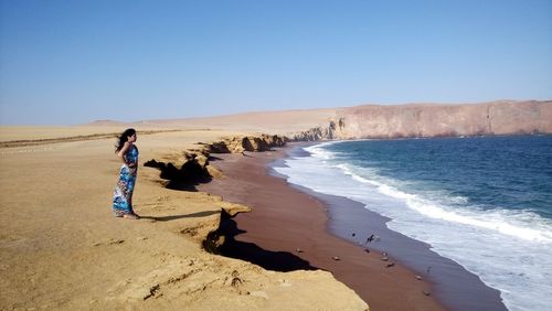 Woman standing on sand at beach against clear sky