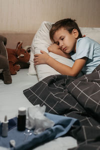 Tired ill child laying in bed with close eyes. some medicines are nearby