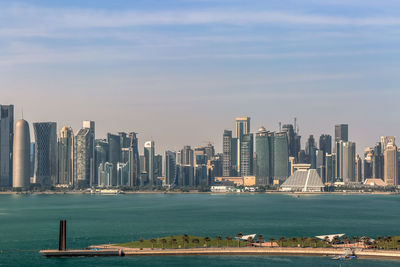 Sea by modern buildings against sky in city