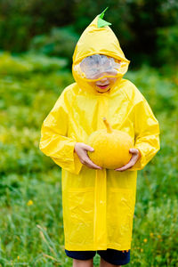Boy in a yellow raincoat holds a yellow pumpkin. preparing for halloween. pumpkin harvest