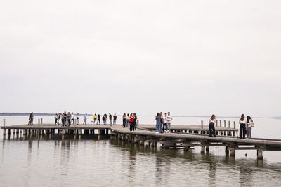 Group of people on pier against clear sky