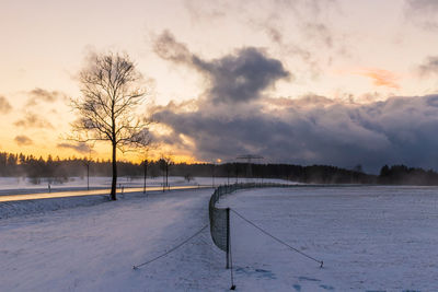 Snow covered field against sky during sunset