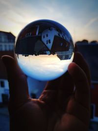 Close-up of hand holding crystal ball against sky