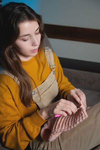 Attractive young woman knits woolen clothes while sitting on the sofa. knitting hook. home hobby