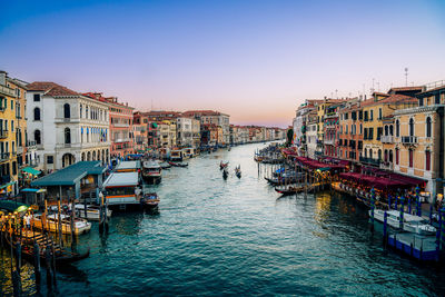 Boats moored in canal in city against clear sky