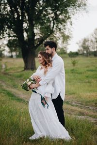 Young couple standing on grass against trees