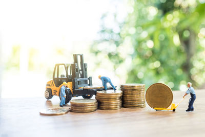 Close-up of figurines with toy forklift with coins on table