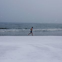 Full length of man jogging on shore at beach against sky