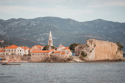 Illuminated buildings by sea against sky