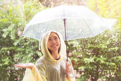 Smiling young woman holding umbrella during rainfall