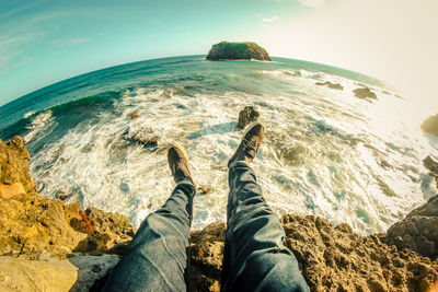 Low section of people on rock by sea against sky