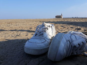 Close-up of shoes on sand at beach against clear sky