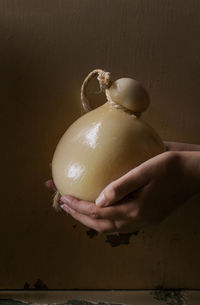 Close-up of hand holding tied up cheese against wall