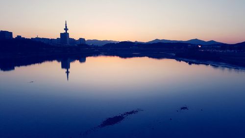 Scenic view of lake by buildings against sky at dusk