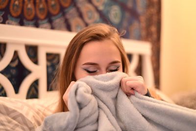 Close-up of teenage girl holding blanket on bed at home