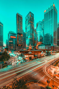 Light trails on city street by buildings against sky