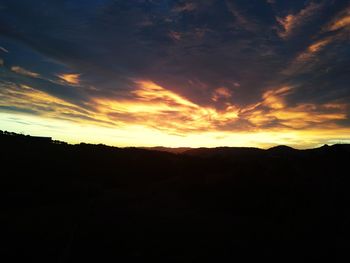 Silhouette landscape against dramatic sky during sunset