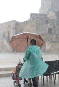 Rear view of woman with umbrella standing outdoors during rainy season