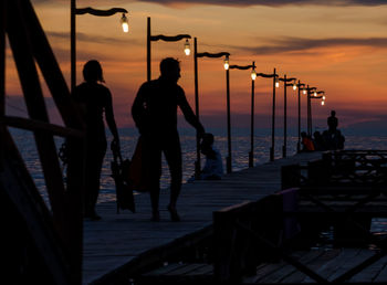 Silhouette people on pier by sea against sky during sunset