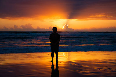 Rear view of silhouette man standing on beach during sunset