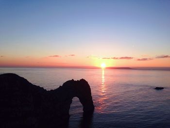 Low section of person on sea at sunset