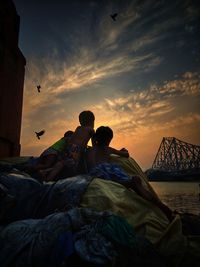 People on shore against sky during sunset