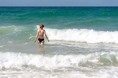 Rear view of carefree woman standing in sea