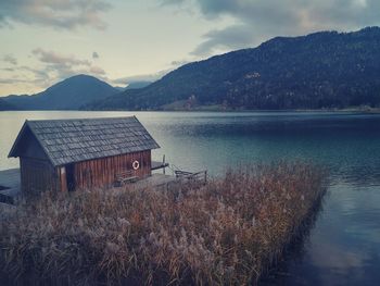 House by lake against sky during sunset