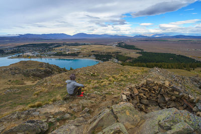 Man sitting on mountain against sky