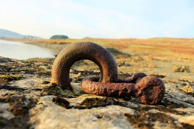 Close-up of rusty bollard ring at lakeshore against sky