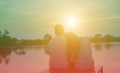 Rear view of men in lake against sky during sunset