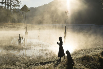 Silhouette woman walking by foggy lake in forest