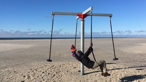 Mother and daughter wearing warm clothing while swinging at beach
