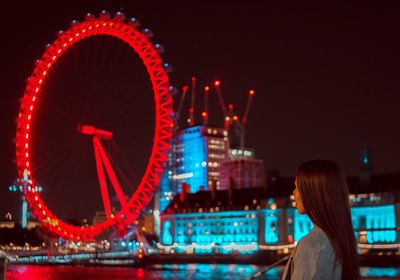 Woman looking at illuminated ferris wheel against sky at night