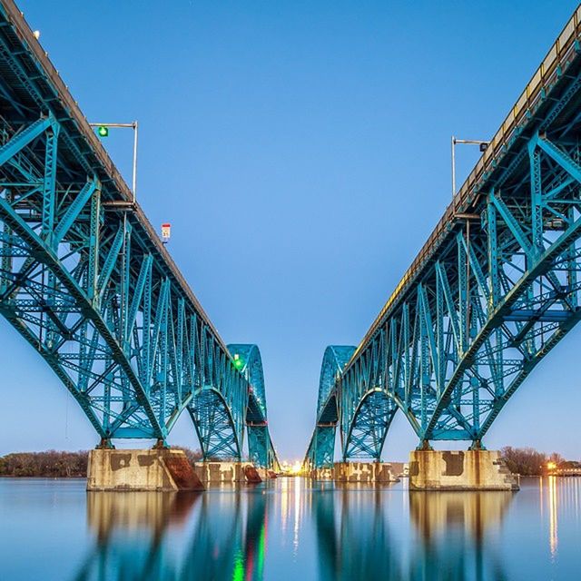 architecture, built structure, clear sky, blue, connection, bridge - man made structure, water, building exterior, reflection, bridge, low angle view, copy space, waterfront, engineering, river, day, city, outdoors, no people, sky