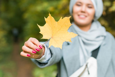 Smiling woman holding autumn leaf at park