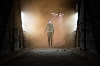 Full length of man holding distress flare while jumping in abandoned workshop