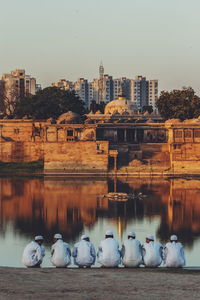 Men crouching by lake against cityscape