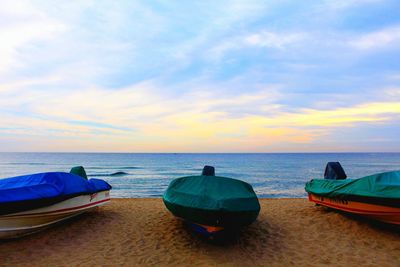 Boats on beach against sky during sunset