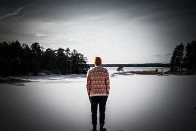 Rear view of man standing by lake against sky