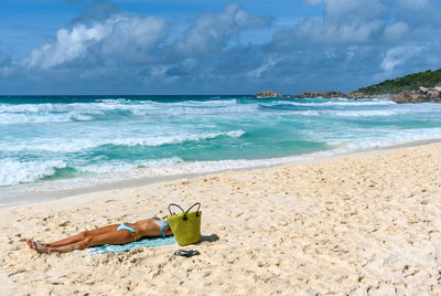 Young woman wearing bikini, laying on towel and sunbathing on tropical sandy beach