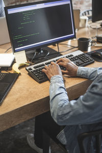 Midsection of male hacker coding on computer at office