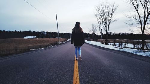 Rear view of woman walking on road against sky