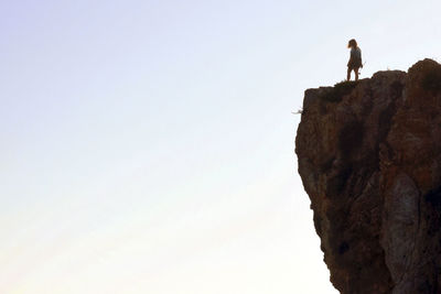 Low angle view of man standing on rock against sky